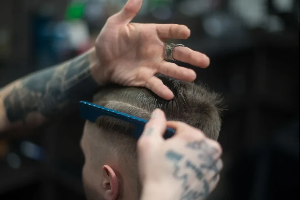 Close-up of a tattooed barber holding a comb and styling a client's neat, side-parted hair